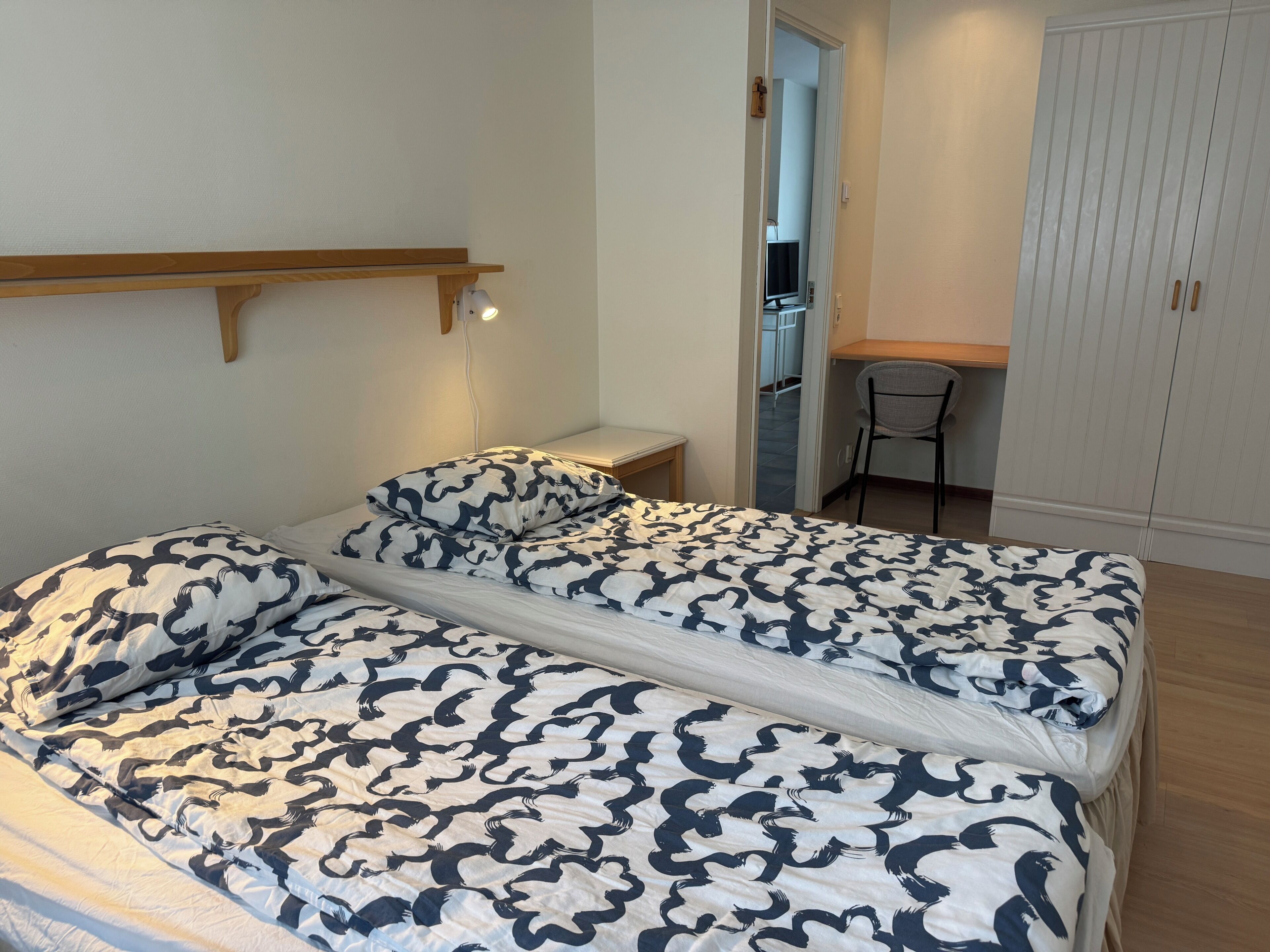 A bedroom with a bed, a desk, and a wardrobe.