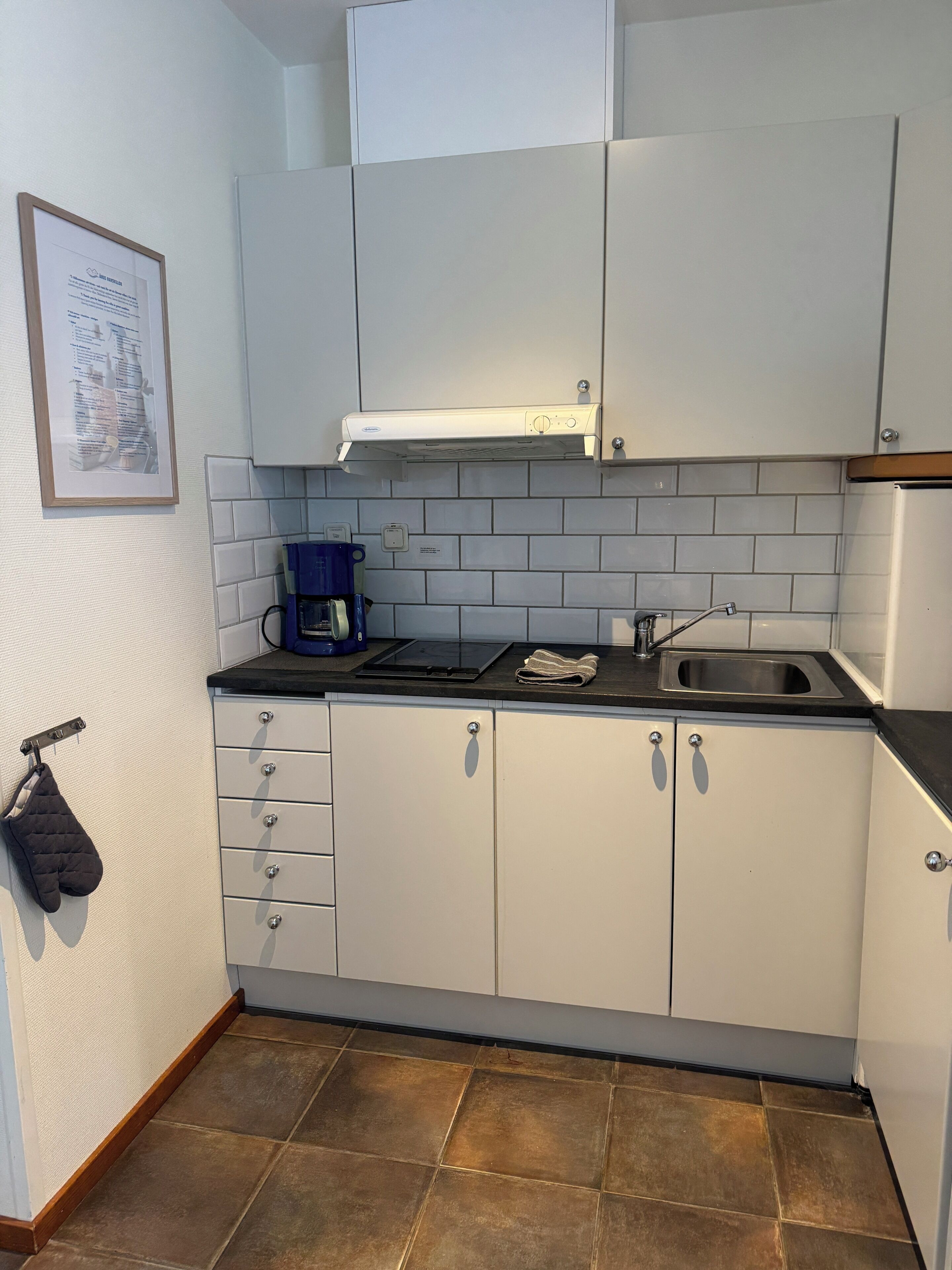 A kitchen with white cabinets, a stainless steel sink, and a blue coffee maker.