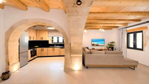 A modern interior with an arched doorway leading to a kitchen, a sofa in a living area, and a large window with curtains.