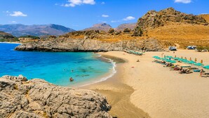 A beach with clear turquoise water, rocky cliffs, and a row of beach umbrellas.