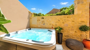 A hot tub with a stone wall and potted plants in a sunny outdoor setting.