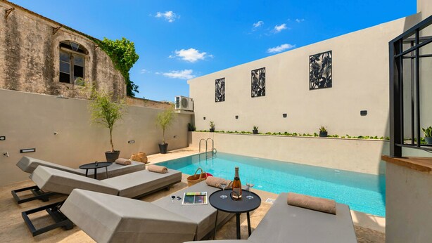 A poolside area with lounge chairs, a table with a bottle and glasses, and a pool.