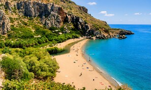 A beach with clear blue water, a sandy shore, and rocky cliffs.