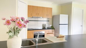 A modern kitchen with wooden cabinets, a stainless steel sink, and a white refrigerator. - Riverview Modern Haven | Entire 4BR Home (Riverview)