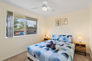 A bedroom with a bed, two bedside tables with lamps, a ceiling fan, a window with a view, and two framed pictures on the wall. - Riverview Modern Haven | Entire 4BR Home (Riverview)
