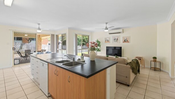 A modern kitchen with a central island, a dining area with a sofa, and a TV in a living room. - Riverview Modern Haven | Entire 4BR Home (Riverview)