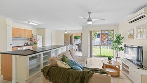 A modern kitchen with a central island, a dining area with a sofa, and a TV on a stand. - Riverview Modern Haven | Entire 4BR Home (Riverview)