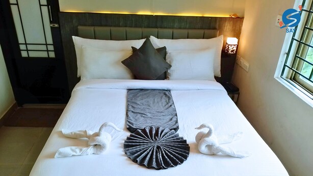 A neatly made bed with white linens, a grey throw, and decorative swan and rabbit towels. - Say Moments (Kolkata)