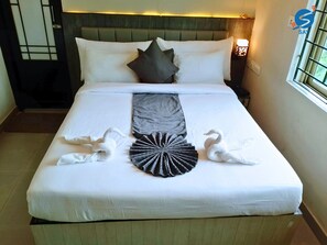 A neatly made bed with white linens, a grey throw, and decorative swan and rabbit towels. - Say Moments (Kolkata)