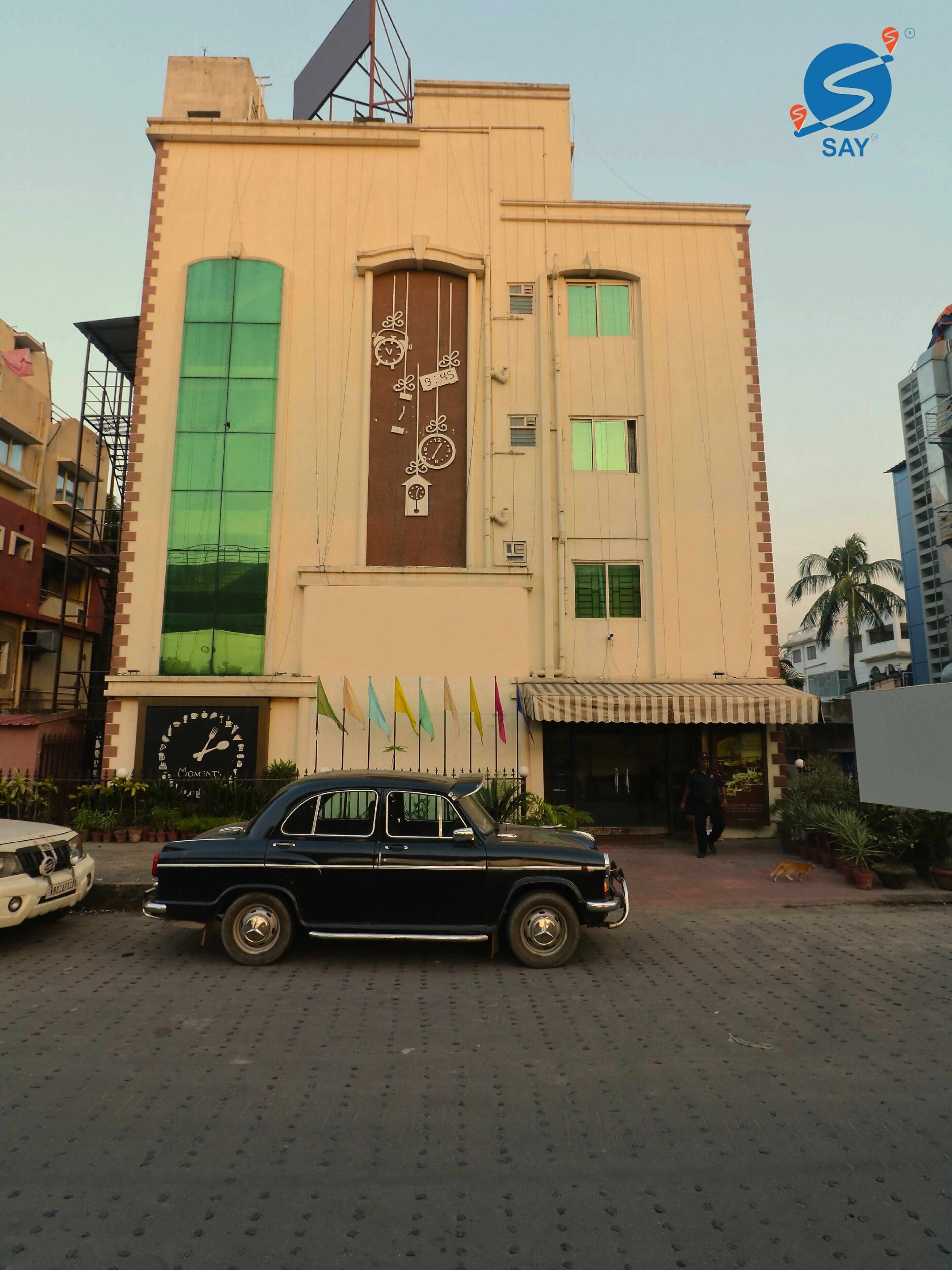 Un edificio con una torre dell'orologio sulla facciata, un'auto parcheggiata e una persona che cammina.