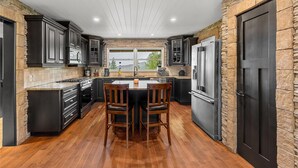 A modern kitchen with dark cabinetry, a central island, and a stone accent wall.