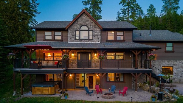 A two-story house with a stone facade, a balcony, and a patio area with outdoor seating.