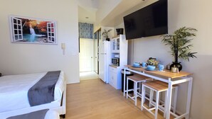 Una habitación compacta con cama, kitchenette pequeña, televisión y zona de comedor.