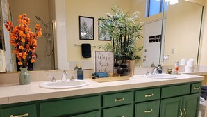 Un baño con dos lavamanos, muebles de color verde, un espejo grande, una planta en maceta y un letrero que dice "Wash Sock Relax".