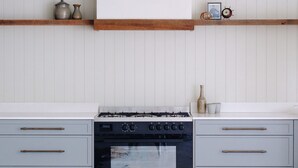 A kitchen with a stove, oven, and two drawers. There are shelves above the counter with decorative items. - Skippers Hideaway - A Peaceful Coastal Escape (The Entrance North)