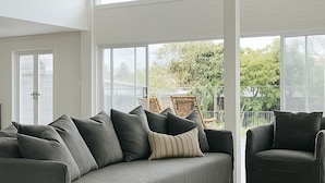 A spacious living room with a grey sofa, a dark armchair, and a woven rug. - Skippers Hideaway - A Peaceful Coastal Escape (The Entrance North)