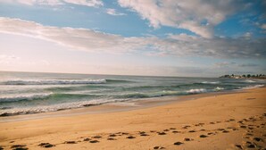 A beach with footprints leading to the water, waves, and a distant shoreline with buildings. - Skippers Hideaway - A Peaceful Coastal Escape (The Entrance North)