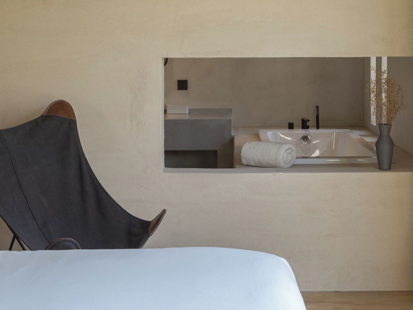 A modern bedroom with a large bed, a chair, a small bathroom with a sink and towel.