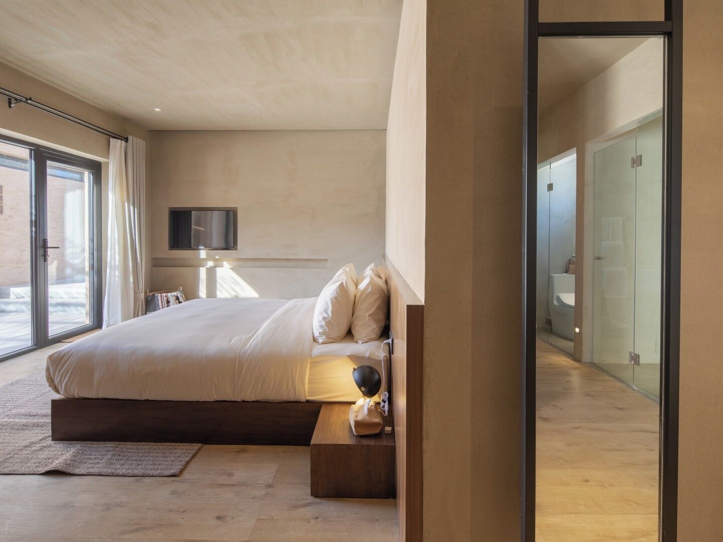 A modern bedroom with a large bed, a flat-screen TV, and a view of the outdoors.