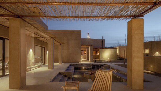 Un espacio exterior moderno con estructura de concreto, un pequeño elemento acuático y una silla de madera.