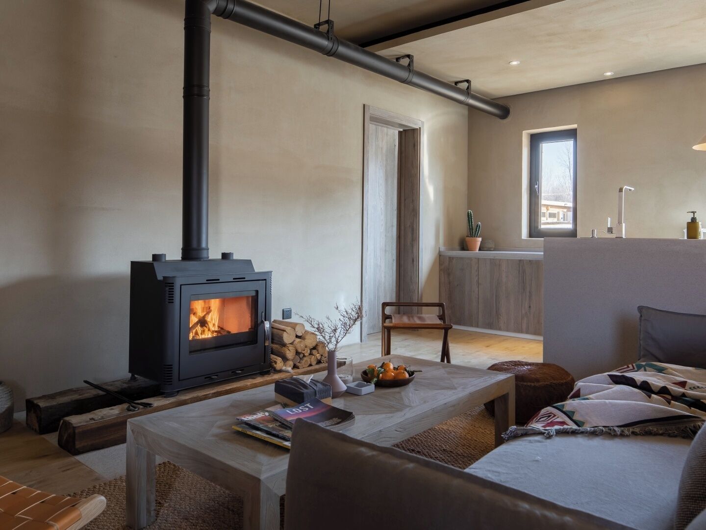 A cozy living room with a wood-burning stove, a dining area, and a kitchen with a window.