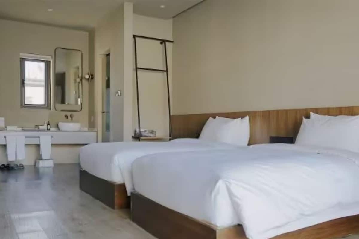 Une chambre d’hôtel moderne avec un grand lit, une table de chevet et une salle de bain équipée d’un miroir et d’un lavabo.