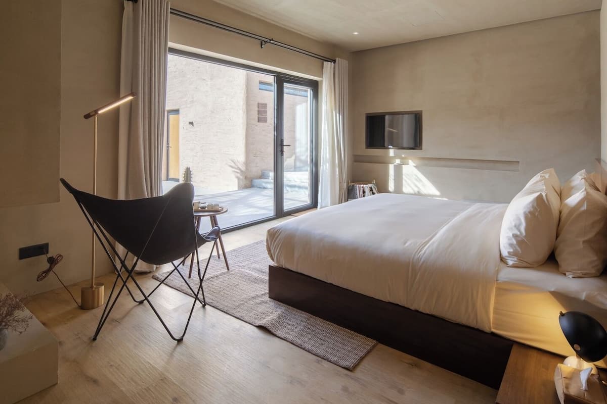 Une chambre d’hôtel moderne, dotée d’un grand lit, d’un fauteuil, d’une télévision et offrant une vue sur l’extérieur.