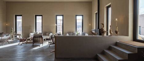 A spacious living area with a central island, large windows, and a staircase leading to an upper level.