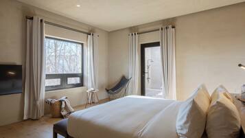Un dormitorio con una cama grande, una silla, un televisor y una ventana con cortinas.