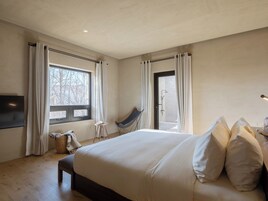 Un dormitorio con una cama grande, una silla, un televisor y una ventana con cortinas.