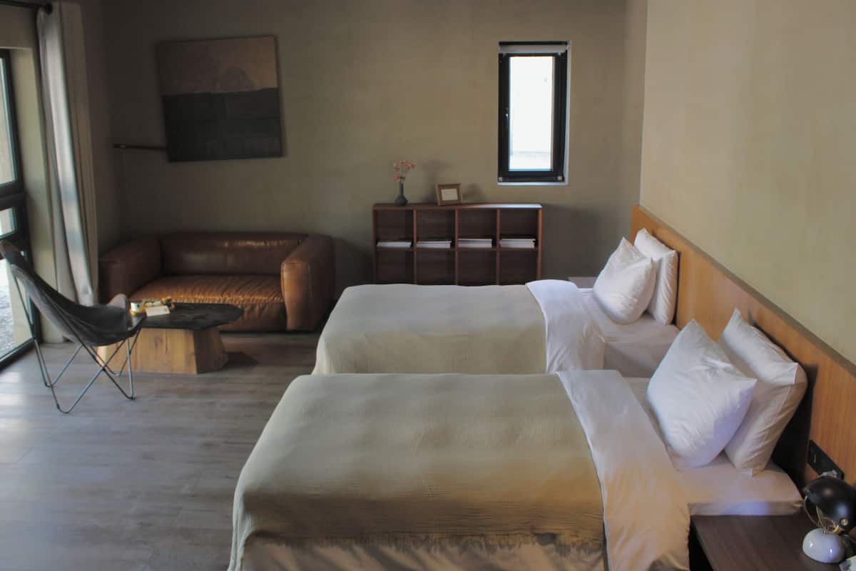 Une chambre d’hôtel avec deux lits, un canapé, une petite table, une bibliothèque et une fenêtre.