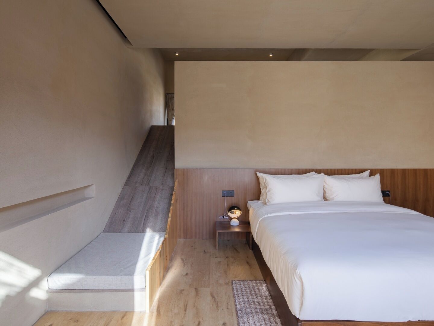 A modern bedroom with a large bed, a nightstand, and a wooden staircase.