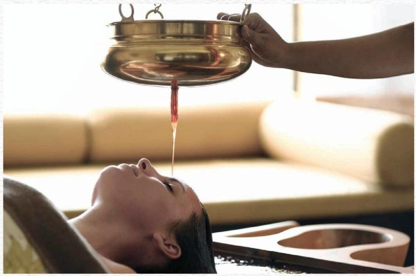 Una persona acostada con un cuenco metálico sobre la cabeza, posiblemente para un tratamiento de spa.