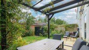 Eine Terrasse mit Tisch und Stühlen, umgeben von Grünpflanzen und einem Holzzaun.