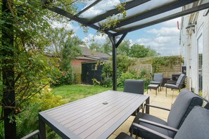 A patio with a table and chairs, surrounded by greenery and a wooden fence. - The Net House | Winterton Cottages (Winterton-on-Sea)