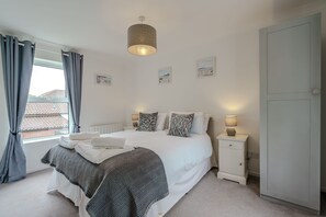 Een slaapkamer met een bed, nachtkastje, lamp en gordijnen.