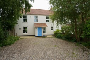 A two-story house with a gravel driveway, a blue door, and a tiled roof. - The Net House | Dog Friendly Coastal Retreat near Winterton Beach (Winterton-on-Sea)