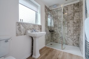 A bathroom with a pedestal sink, a glass-enclosed shower, and a window. - The Net House | Winterton Cottages (Winterton-on-Sea)