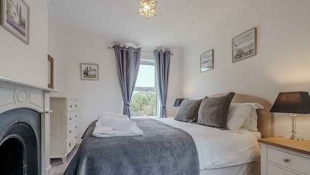 Ein Schlafzimmer mit einem Bett, einem Schminktisch, einer Lampe, einem Kamin und Vorhängen.