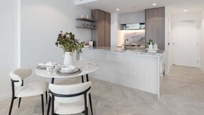Een moderne keuken met een marmeren eiland, witte kasten en een eethoek met twee stoelen.
