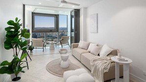 Een moderne woonkamer met een beige bank, een ronde salontafel en een groot raam met uitzicht op de stad.