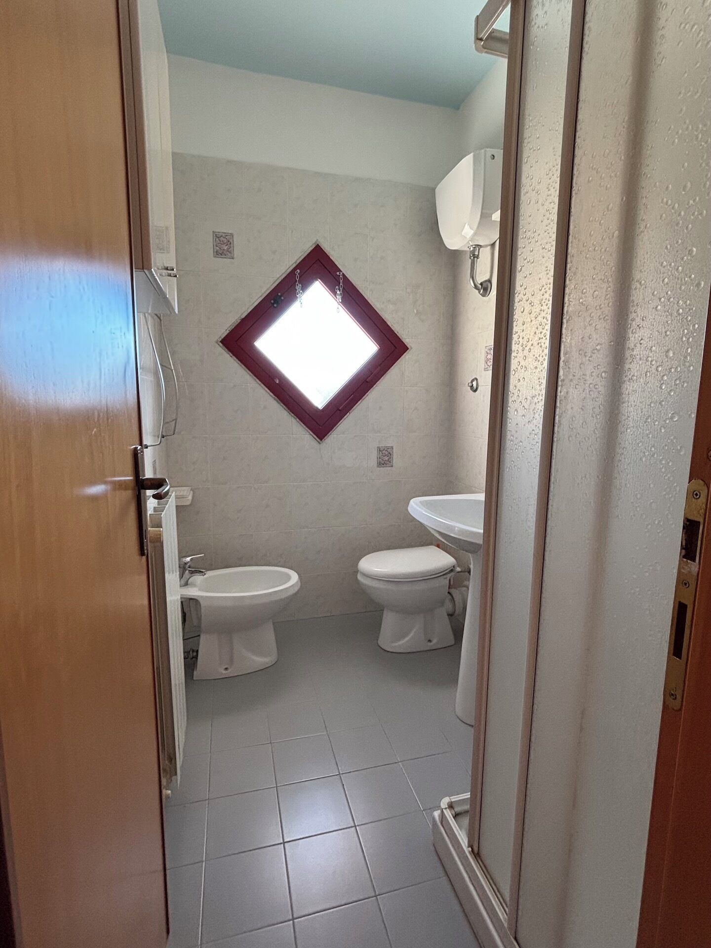 A small bathroom with two toilets, a sink, and a window.