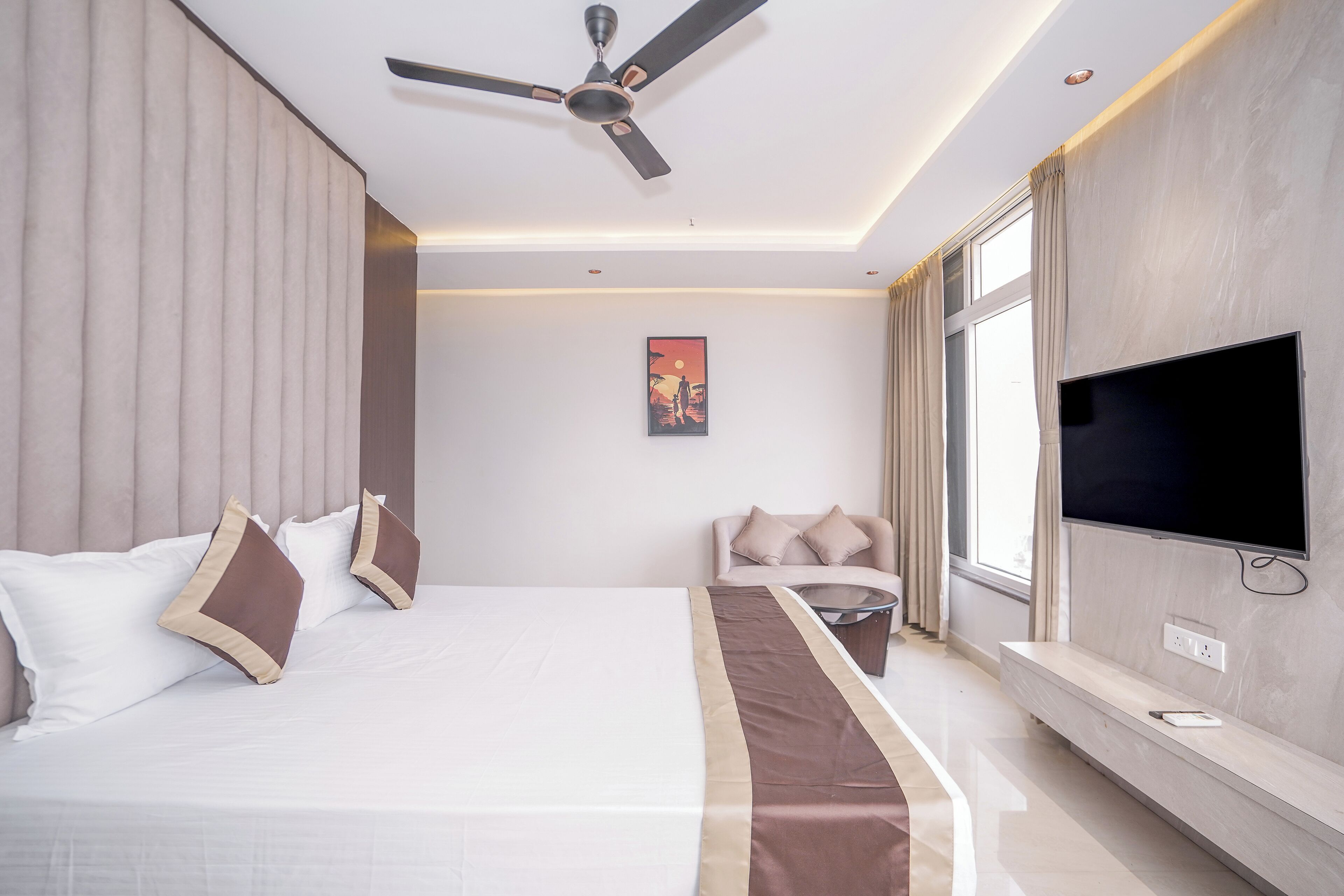A modern hotel room with a large bed, a flat-screen TV, a ceiling fan, and a window with curtains.