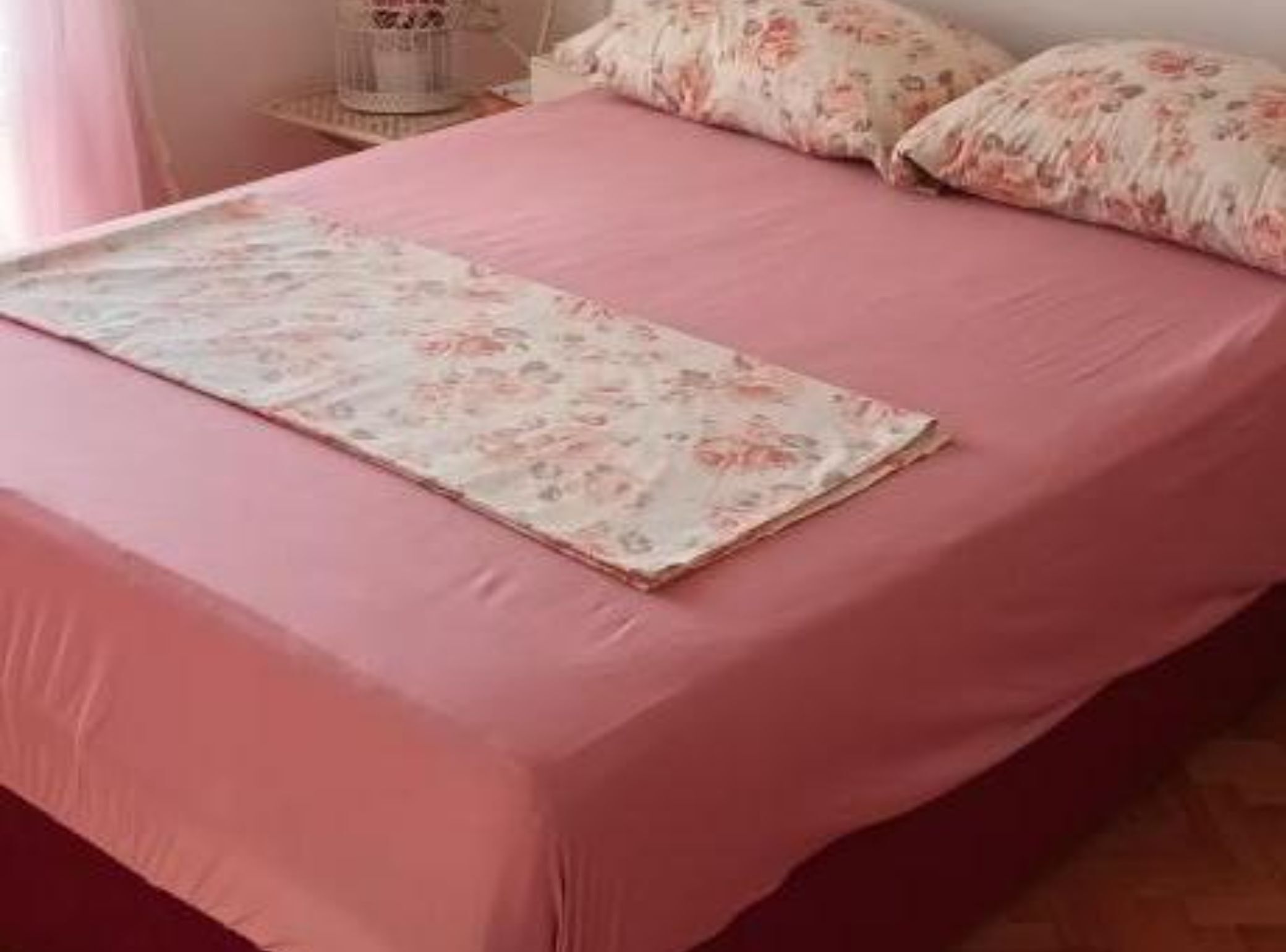 Una cama con una colcha rosa y almohadas estampadas con motivos florales.