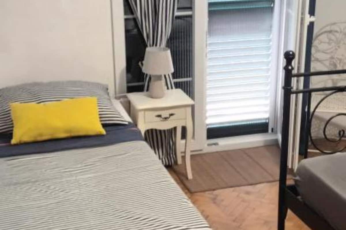 Een slaapkamer met een bed, nachtkastje, lamp en raam met jaloezieën.