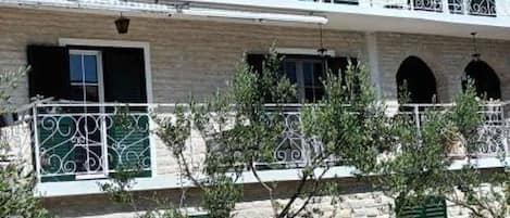 Un immeuble à plusieurs étages, doté de balcons, d’une façade en pierre et de volets verts.