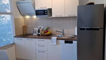A modern kitchen with white cabinets, a stainless steel refrigerator, a microwave, and a fruit bowl on the counter.