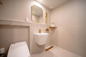 A modern bathroom with a white sink, a gold-framed mirror, and a shower. - Denbasta Hotel Guseo (Busan)