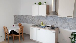 A compact kitchen with white cabinets, a small dining table with chairs, and a potted plant. - Comfort Apartment Baruna Filipovića (Zagreb)
