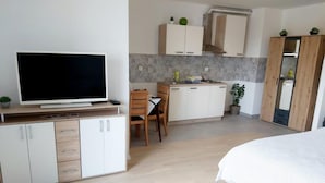 A modern bedroom with a large bed, a TV on a wooden stand, a desk with a chair, and a kitchenette with cabinets and a sink. - Comfort Apartment Baruna Filipovića (Zagreb)